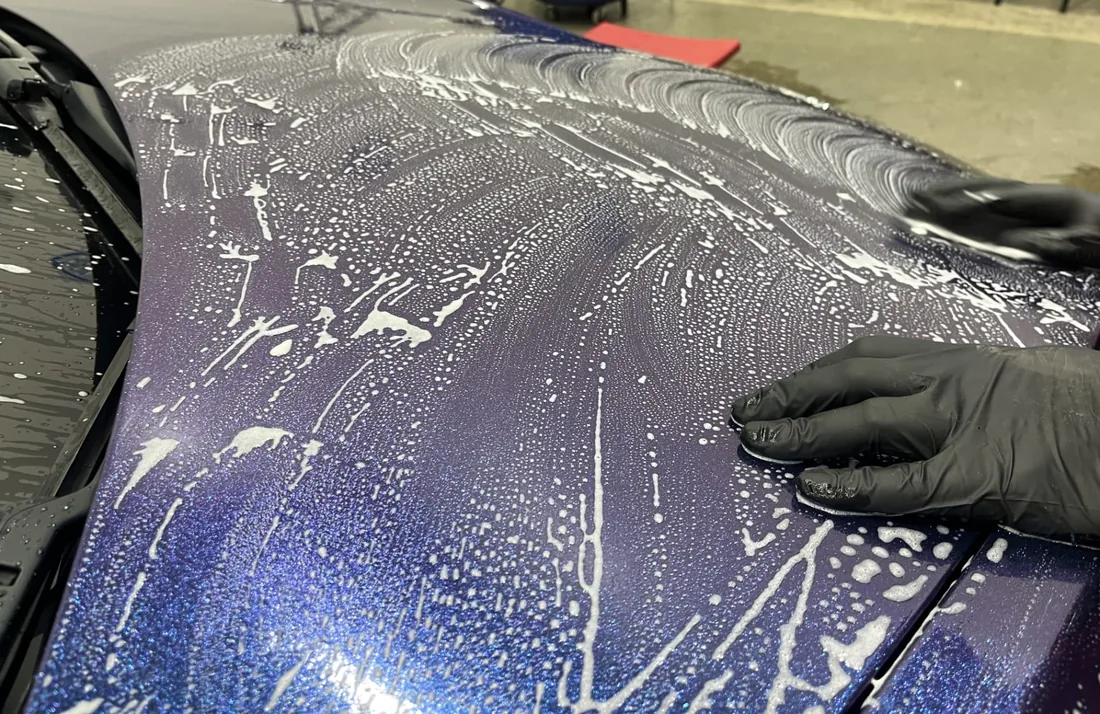 A gloved technician washing and decontaminating a vehicle hood
